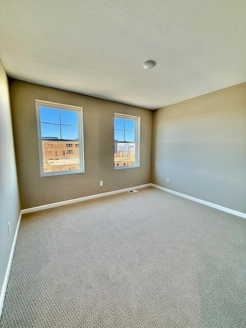 empty room featuring a textured ceiling, carpet flooring, and baseboards