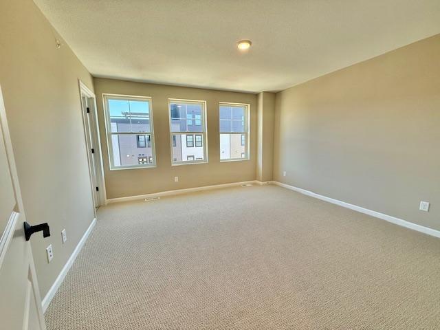 spare room featuring light colored carpet and baseboards