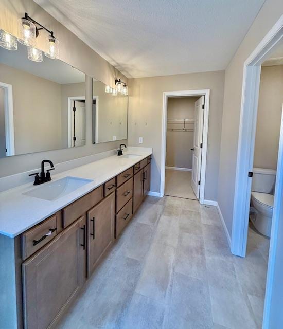 bathroom featuring double vanity, a spacious closet, toilet, and a sink