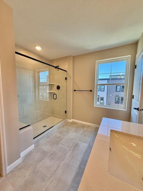 full bathroom with a stall shower, a textured ceiling, and baseboards