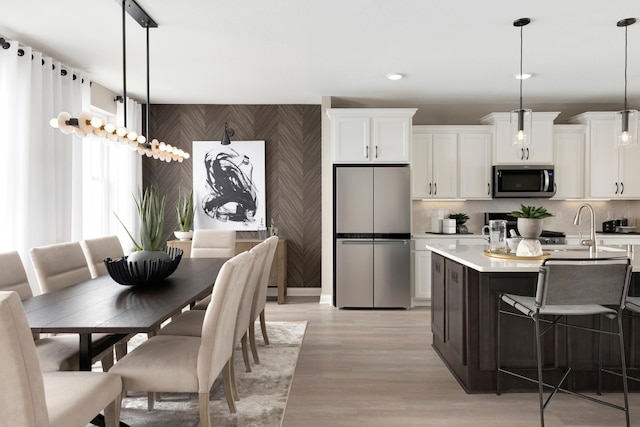 kitchen with wallpapered walls, stainless steel appliances, light countertops, white cabinetry, and an accent wall