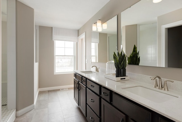 bathroom with baseboards, tile patterned flooring, double vanity, and a sink