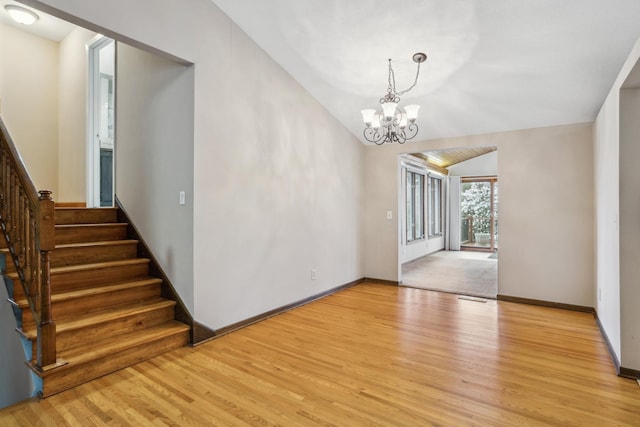 unfurnished room with lofted ceiling, baseboards, stairway, light wood-type flooring, and a chandelier