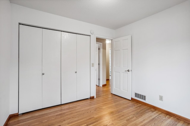unfurnished bedroom featuring baseboards, light wood-style flooring, visible vents, and a closet