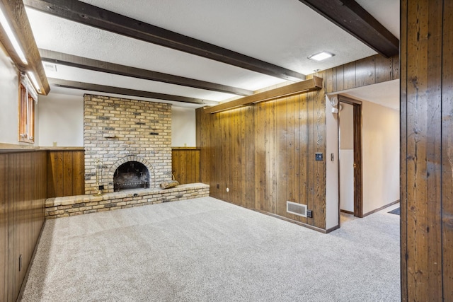 unfurnished living room with visible vents, a brick fireplace, wood walls, carpet floors, and beamed ceiling