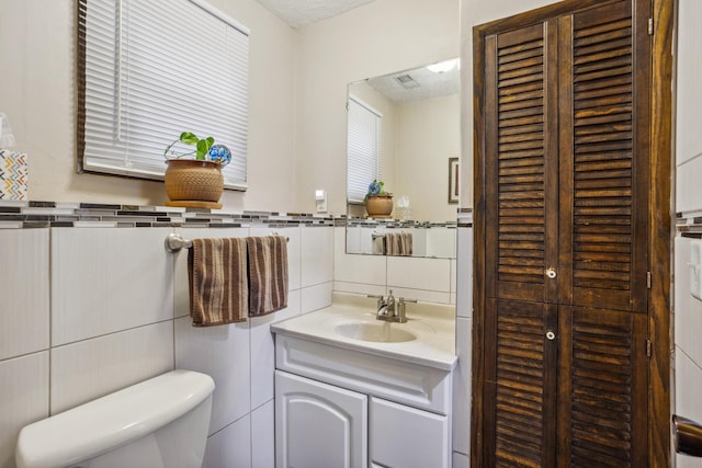 half bath featuring tile walls, vanity, and toilet