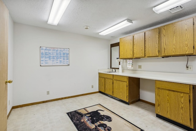 kitchen with visible vents, light floors, light countertops, a textured ceiling, and a sink