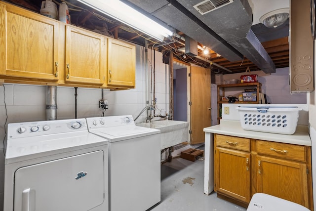 clothes washing area featuring visible vents, washing machine and clothes dryer, a sink, cabinet space, and concrete block wall