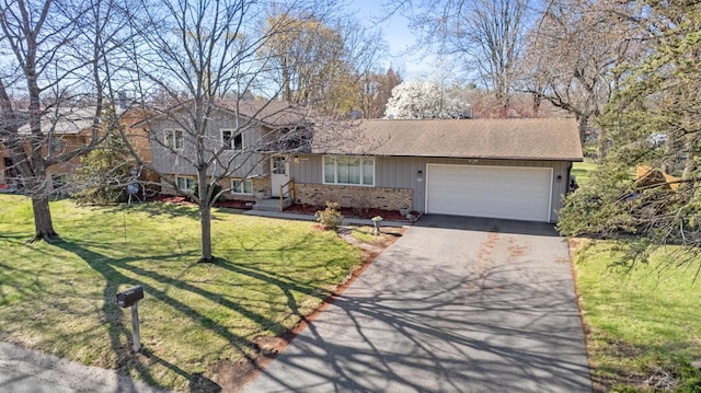 tri-level home with a garage, aphalt driveway, a front yard, brick siding, and a shingled roof