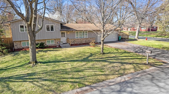 split level home with fence, an attached garage, a front lawn, aphalt driveway, and brick siding
