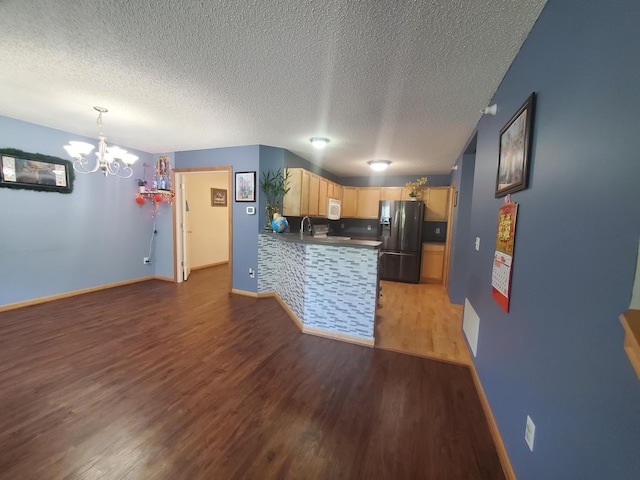 kitchen with a textured ceiling, a chandelier, black refrigerator with ice dispenser, light wood finished floors, and a peninsula