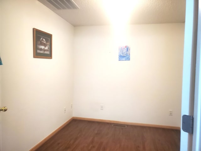 empty room with visible vents, dark wood-style flooring, a textured ceiling, and baseboards