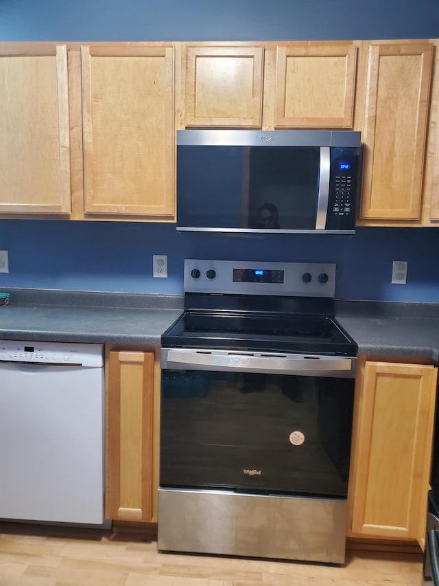 kitchen with stainless steel appliances, dark countertops, light brown cabinets, and light wood-style flooring