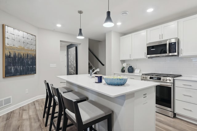 kitchen featuring light wood finished floors, stainless steel appliances, white cabinetry, visible vents, and a center island with sink