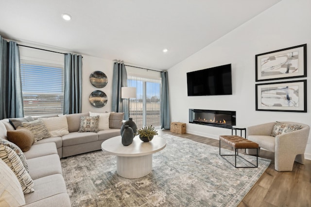 living room featuring recessed lighting, vaulted ceiling, a glass covered fireplace, and wood finished floors