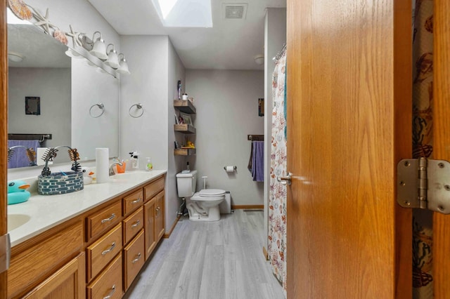 bathroom featuring double vanity, a skylight, wood finished floors, a sink, and toilet