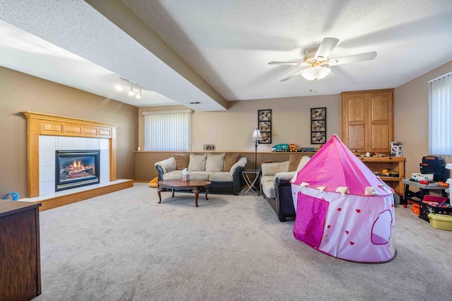 living room featuring carpet floors, a ceiling fan, a textured ceiling, and a tiled fireplace