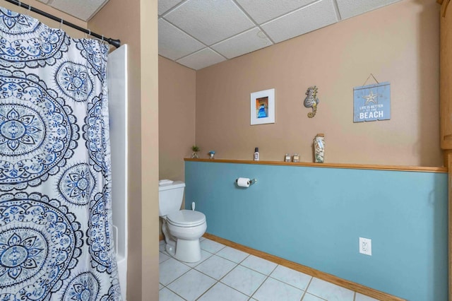 full bath featuring tile patterned floors, a shower with shower curtain, toilet, and a paneled ceiling