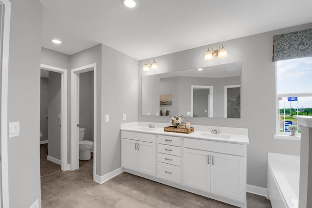 bathroom with double vanity, toilet, baseboards, and a sink