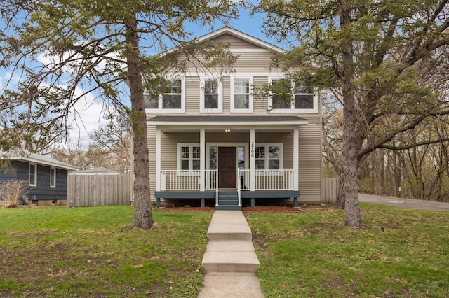traditional-style house with fence, a porch, and a front lawn