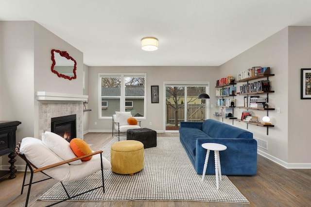 living area featuring a tile fireplace, visible vents, wood finished floors, and baseboards