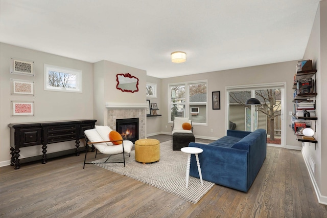 living room featuring a wealth of natural light, wood finished floors, a tiled fireplace, and baseboards