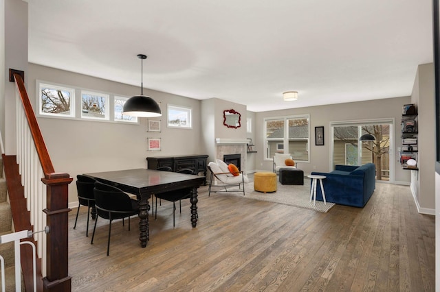 dining room with wood-type flooring, stairway, a tiled fireplace, and baseboards