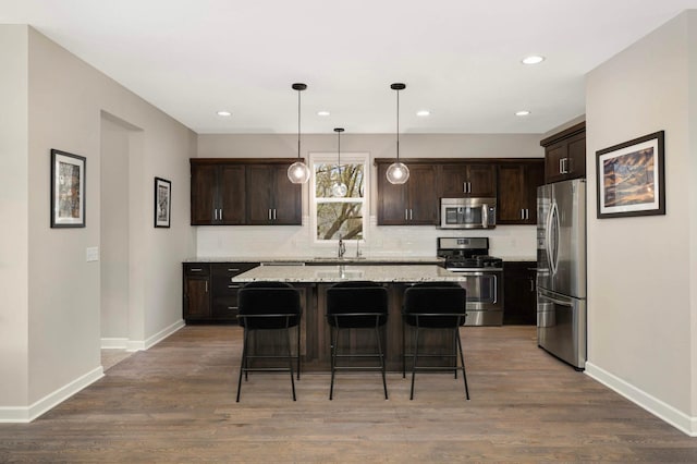 kitchen featuring baseboards, stainless steel appliances, dark brown cabinets, and a breakfast bar