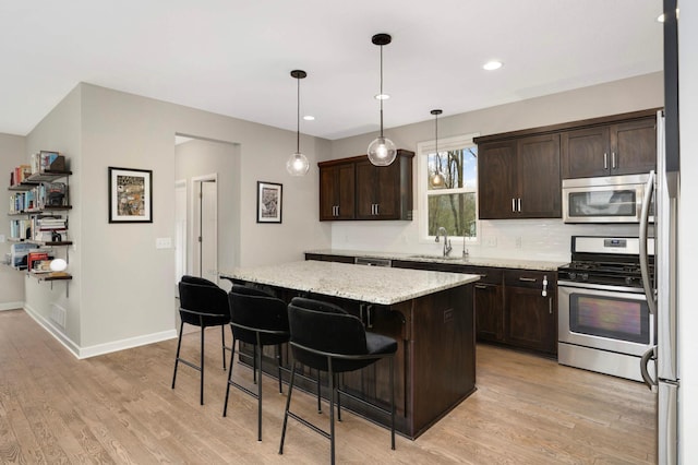 kitchen with dark brown cabinetry, light wood-style flooring, stainless steel appliances, a kitchen island, and a sink