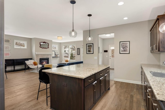 kitchen with dark wood finished floors, a breakfast bar, a glass covered fireplace, dark brown cabinets, and a sink