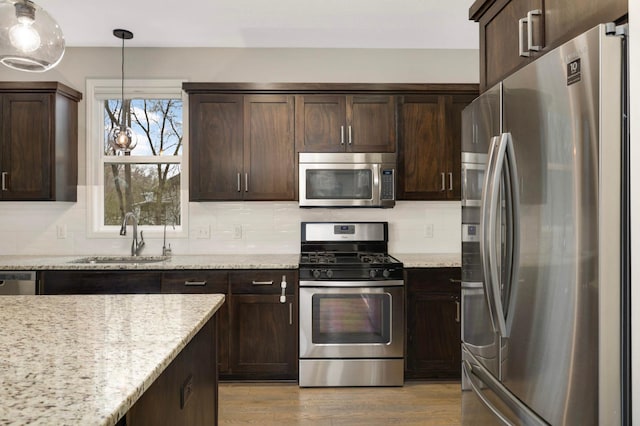 kitchen with dark brown cabinetry, a sink, decorative light fixtures, and appliances with stainless steel finishes