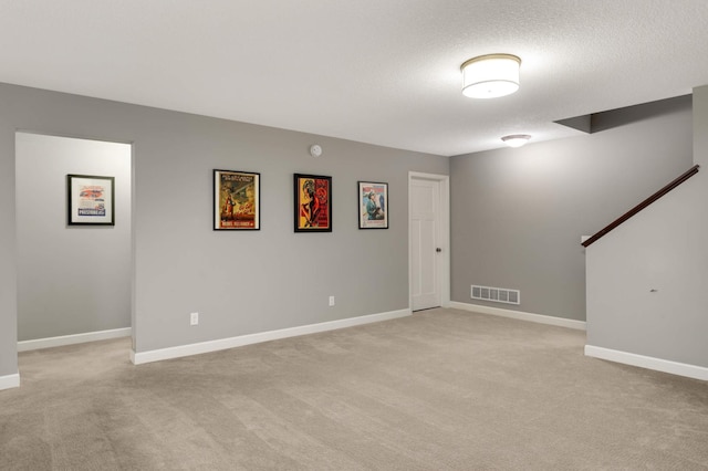 basement featuring a textured ceiling, visible vents, light carpet, and baseboards