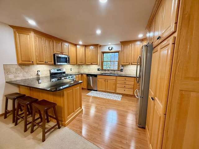 715 Crest Ln, Ellsworth, WI 54011 - kitchen featuring stainless steel appliances, a peninsula, light wood finished floors, a sink, and decorative backsplash