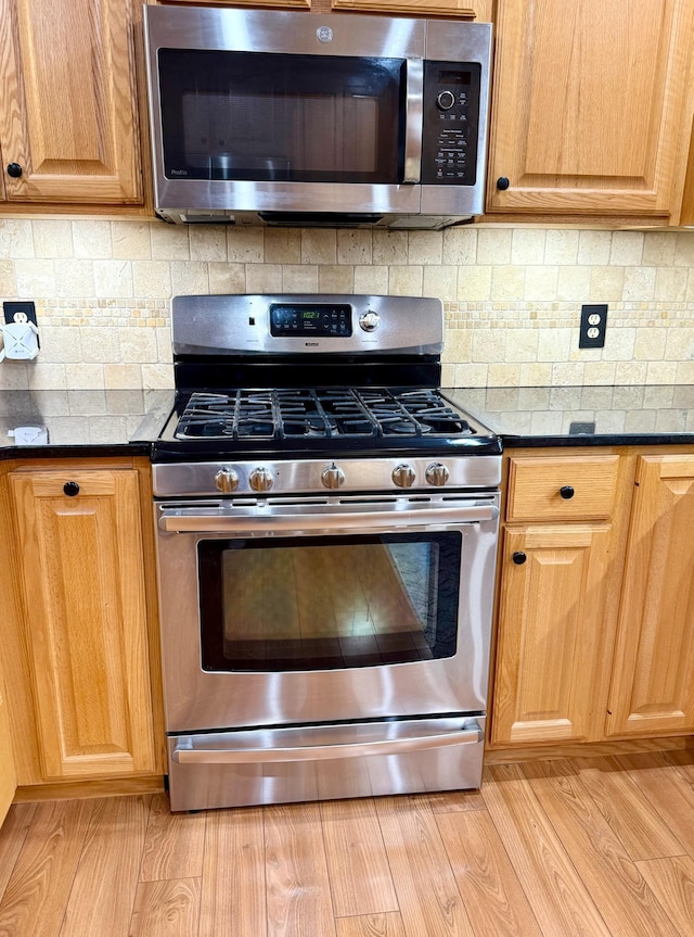 715 Crest Ln, Ellsworth, WI 54011 - kitchen with appliances with stainless steel finishes, dark countertops, light wood finished floors, and decorative backsplash