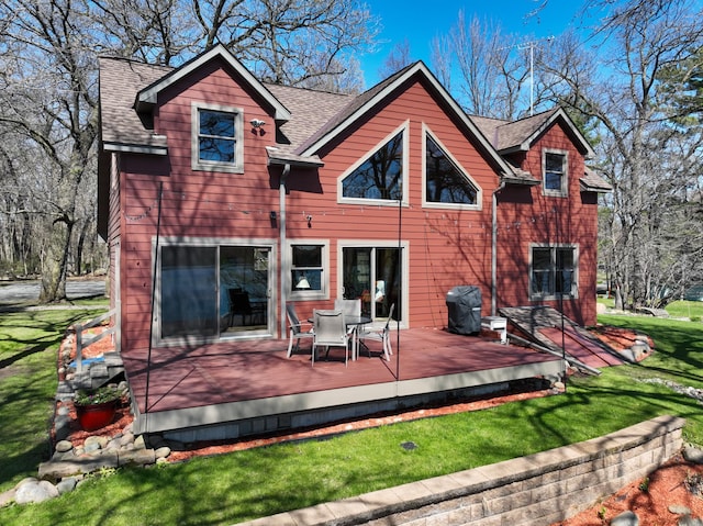 back of property with a shingled roof, a deck, a lawn, and outdoor dining space