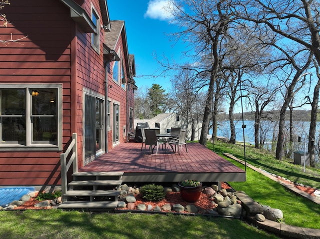 wooden deck with outdoor dining area, a water view, and a lawn
