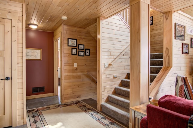 entryway with wooden ceiling, baseboards, visible vents, stairs, and wooden walls