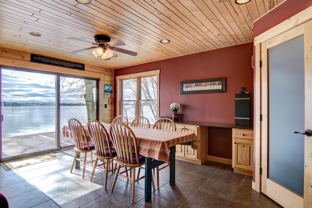 dining room with a water view, dark tile patterned flooring, ceiling fan, and wooden ceiling