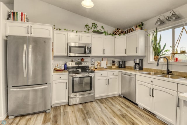 kitchen featuring a sink, white cabinets, stainless steel appliances, and lofted ceiling