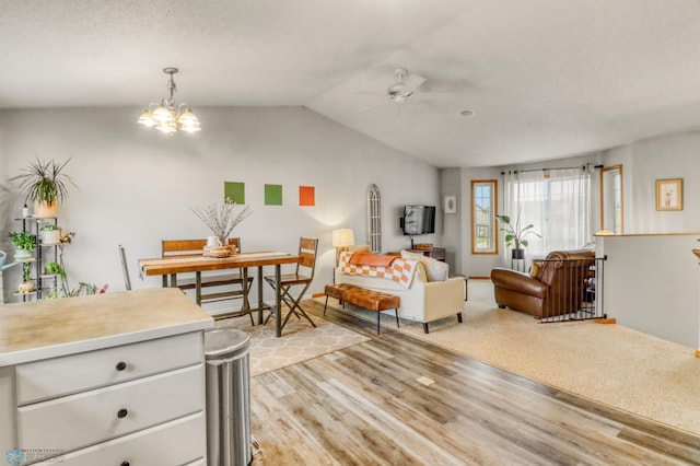 living room featuring light wood-style flooring, ceiling fan with notable chandelier, and lofted ceiling