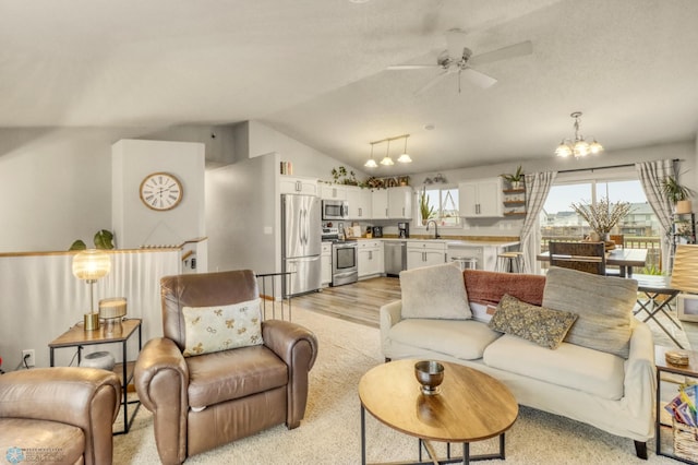 living area with vaulted ceiling, light wood finished floors, and ceiling fan with notable chandelier