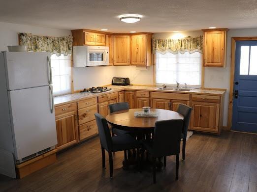 kitchen with white appliances, dark wood-style flooring, light countertops, and a sink