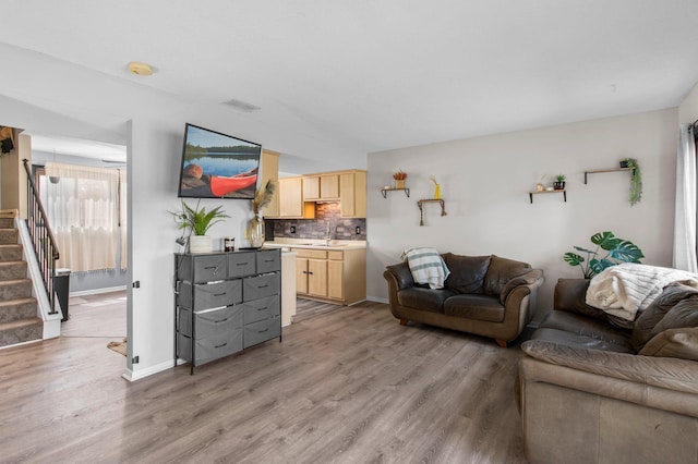 living room featuring baseboards, visible vents, stairway, and light wood-type flooring