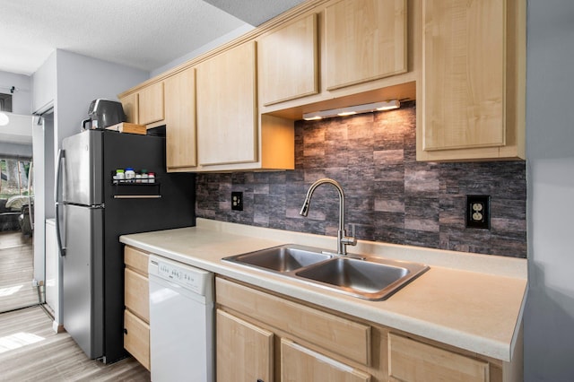 kitchen featuring decorative backsplash, a sink, light countertops, white dishwasher, and light brown cabinetry