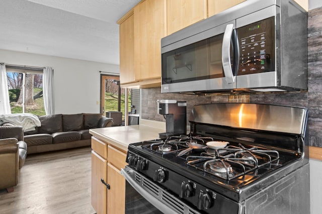 kitchen with light brown cabinets, light wood-style flooring, decorative backsplash, stainless steel appliances, and light countertops