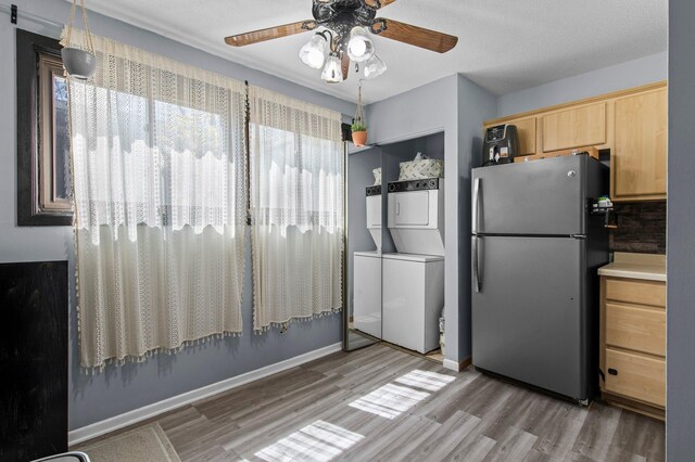kitchen featuring stacked washing maching and dryer, light wood-type flooring, light brown cabinetry, a ceiling fan, and freestanding refrigerator