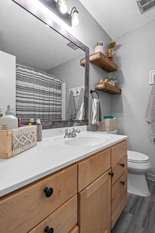 bathroom with wood finished floors, toilet, vanity, visible vents, and a textured ceiling
