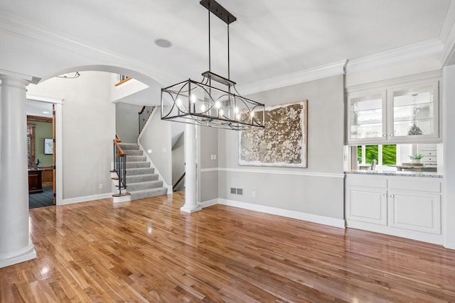 unfurnished dining area with crown molding, visible vents, stairs, light wood-style floors, and ornate columns