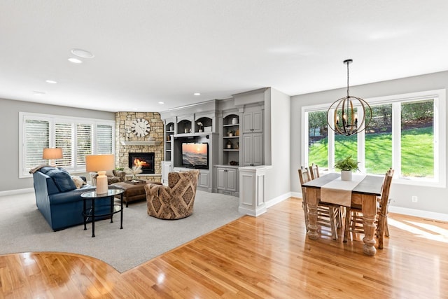 living room with a stone fireplace, baseboards, light wood finished floors, an inviting chandelier, and recessed lighting