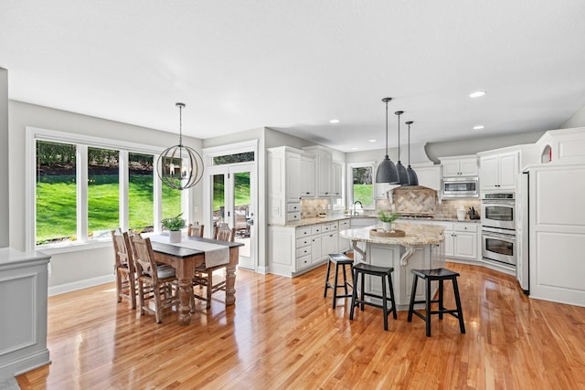 dining room featuring baseboards, plenty of natural light, light wood finished floors, and a notable chandelier